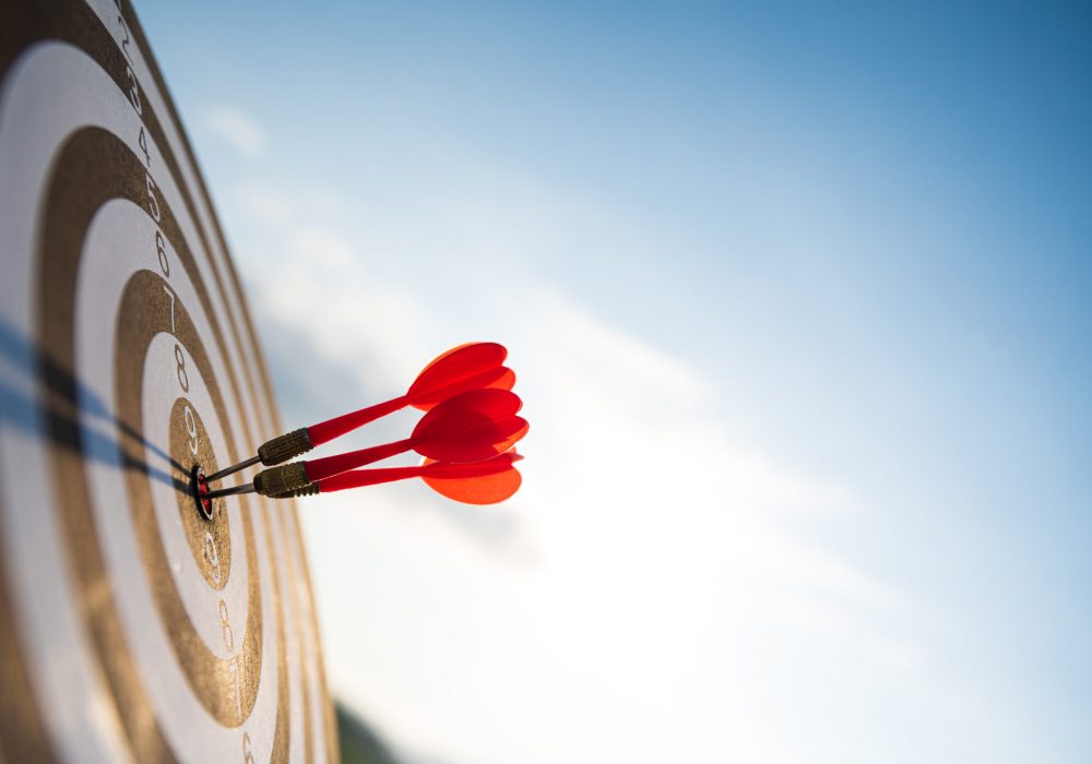 Close up shot red darts arrows in the target center on dark blue sky background. Business target or goal success and winner concept.